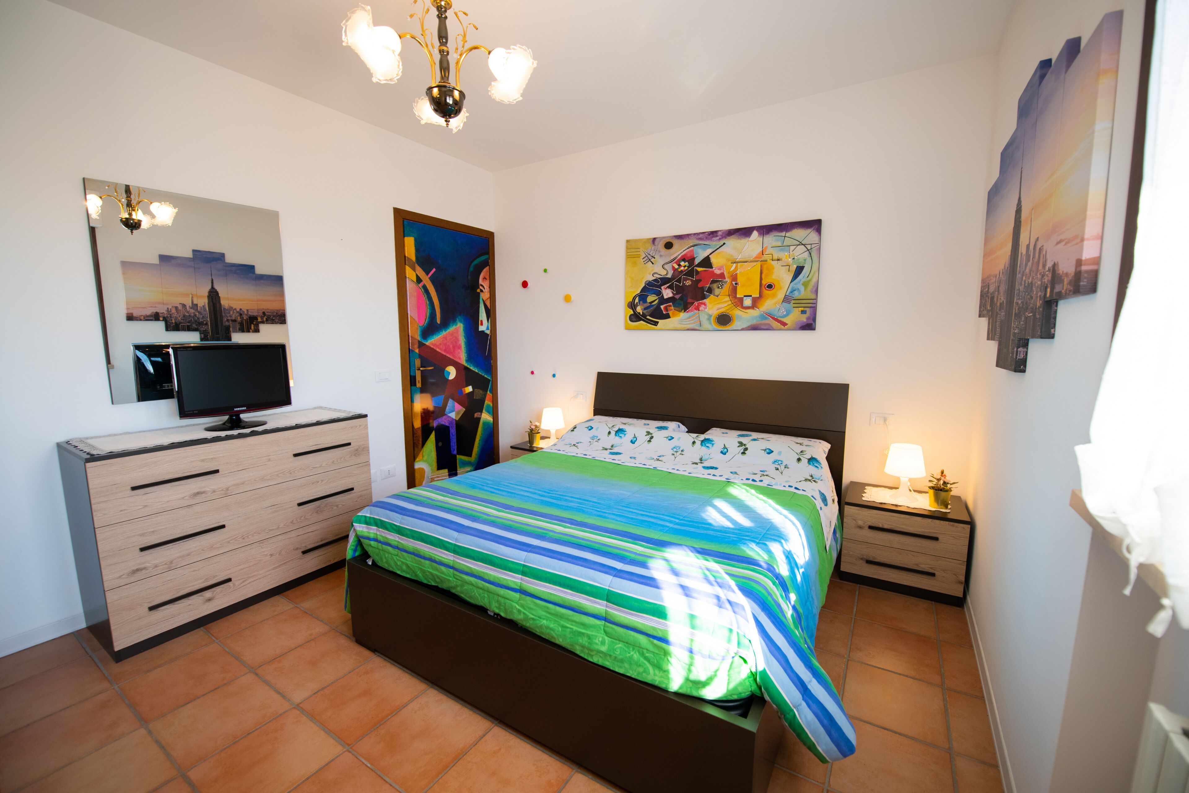 A bedroom with a bed, a dresser, a TV, and artwork on the walls.