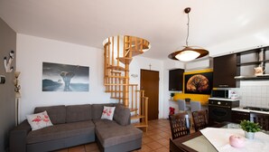A modern living room with a grey sectional sofa, a wooden spiral staircase, and a kitchen area with a microwave and stove. - Appartamento Francesca (Sirmione)