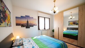 A bedroom with a bed, a window, a radiator, a mirror, and artwork on the walls. - Appartamento Francesca (Sirmione)