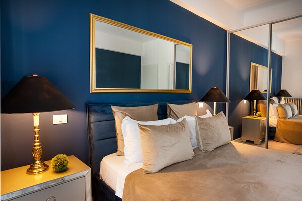 A bedroom with a large bed, two bedside tables with lamps, a mirror, and a small decorative plant.