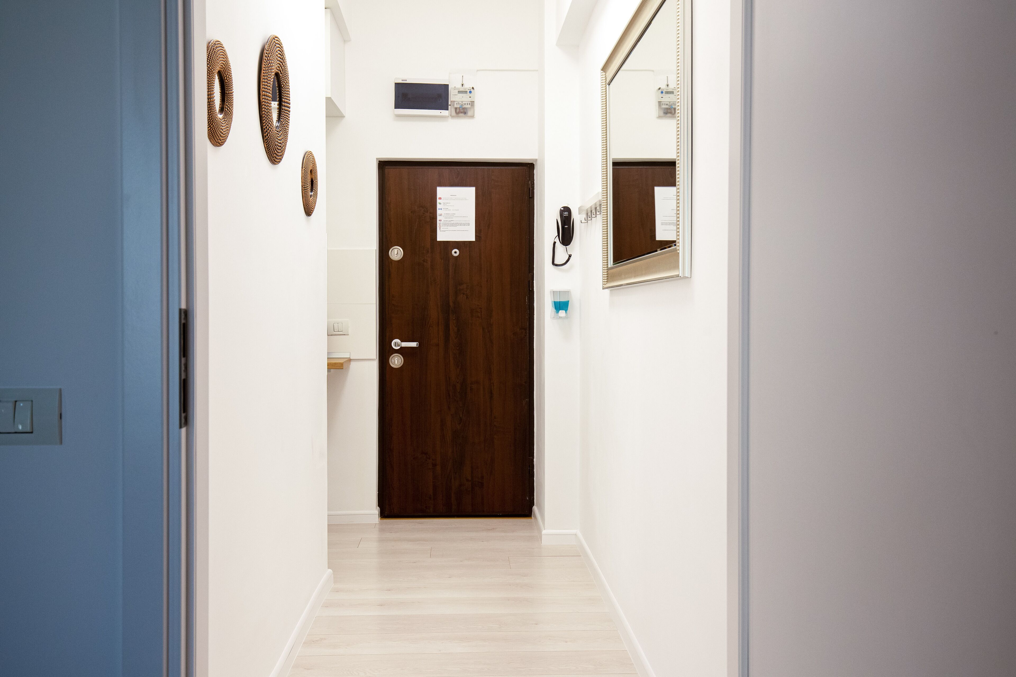 A hallway with a wooden door, a wall-mounted phone, and a mirror.