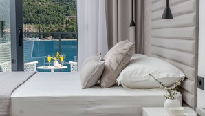 Et soveværelse med en seng, et natbord med en vase og en bog, samt udsigt til en pool og et udendørs loungeområde.