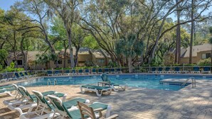 A pool area with lounge chairs and a swimming pool surrounded by trees and buildings.