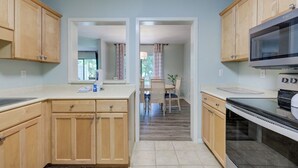 A kitchen with wooden cabinets, a microwave, and a stove. There is a dining area with a table and chairs visible through an open doorway.