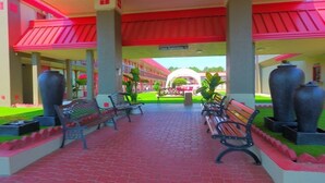 A covered walkway with benches and large vases, leading to a building with a red roof and a sign indicating "Lobby Reception". - Ramada Perry near Fairgrounds (Perry)