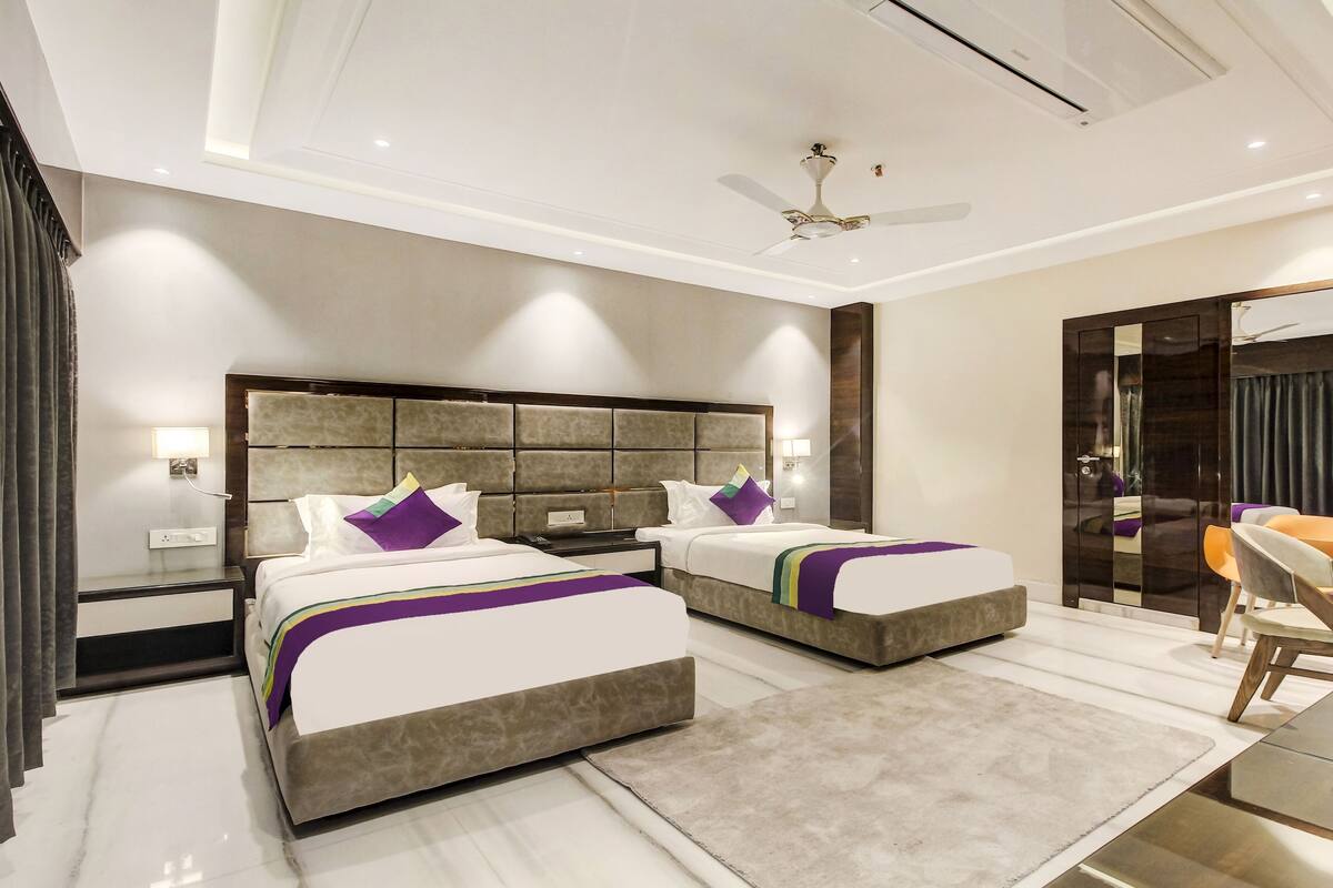 A modern hotel room with two beds, a ceiling fan, and a seating area with a table and chairs.