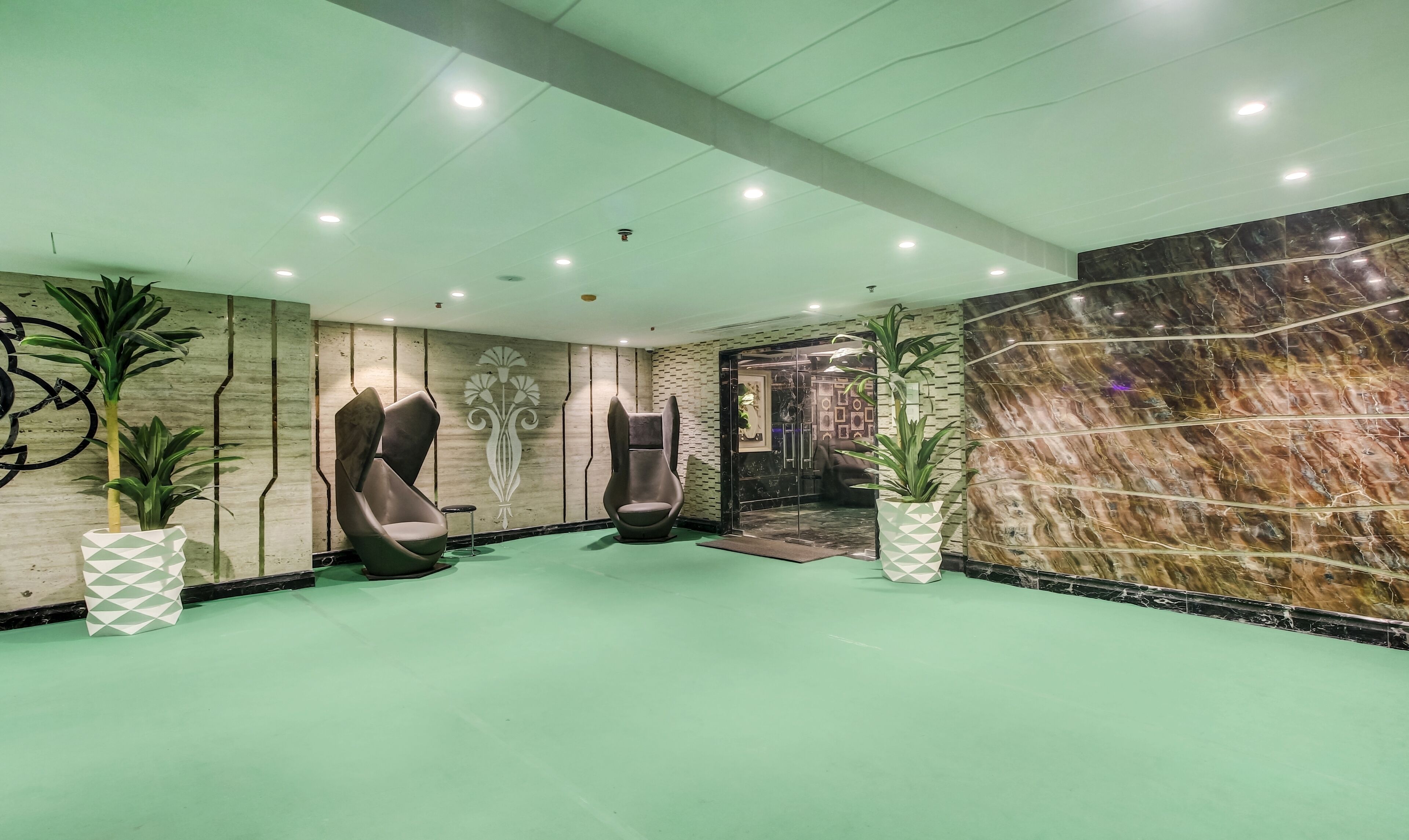 A lobby with two modern chairs, a green floor, and a marble wall.