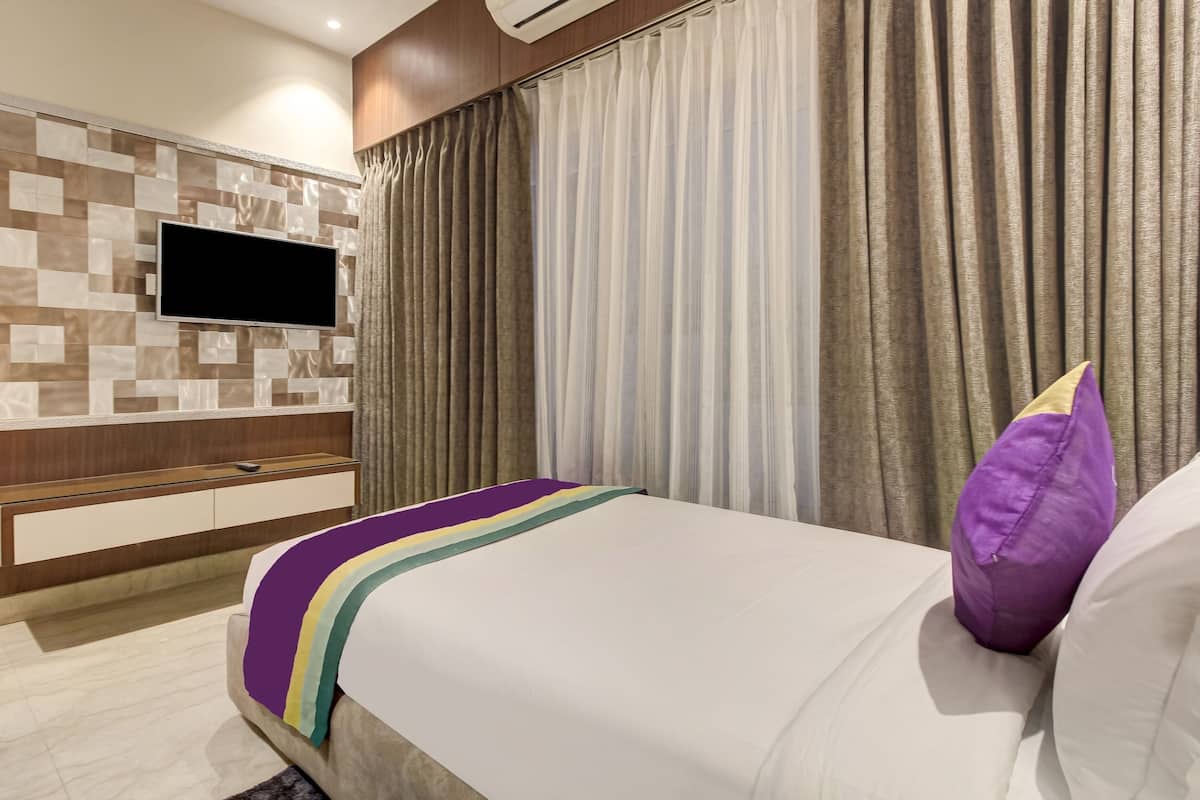 A hotel room with a bed, a TV mounted on a wall, a wooden cabinet, and a window with curtains.