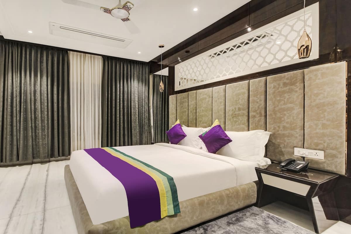 A modern hotel room with a large bed, a bedside table with a phone, and a wall-mounted TV.
