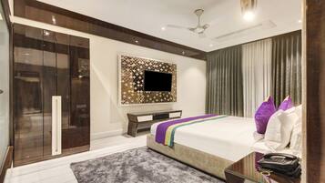 A modern bedroom with a large bed, a TV mounted on a decorative wall, a wardrobe, and a bedside table with a phone.