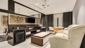 A modern living room with a sofa, coffee table, TV, and a dining area with chairs. - Treebo Premium Tahoora International (Kolkata)