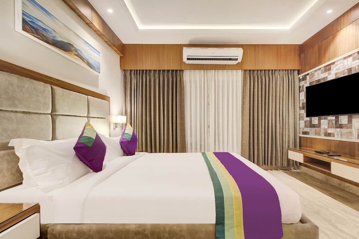 A hotel room with a large bed, a flat-screen TV, a wooden panel wall, and a ceiling-mounted air conditioner.