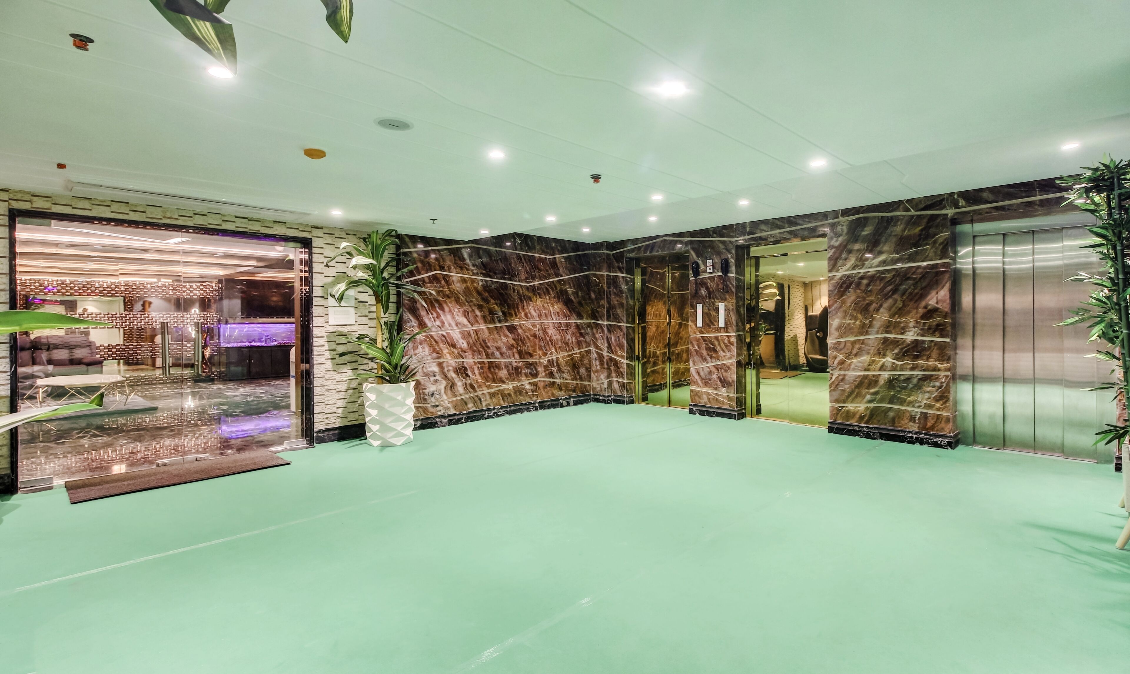 Un vestíbulo con alfombra verde, paredes de mármol y una recepción de diseño moderno.