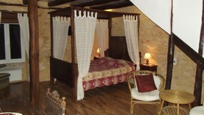 Une chambre à coucher avec un lit à baldaquin, une chaise, une petite table ronde et une table de chevet avec une lampe.