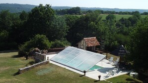 Une maison dotée d’une grande serre en verre, d’une piscine et d’un patio aménagé avec du mobilier d’extérieur.