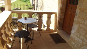 Un petit patio extérieur avec une table ronde et deux chaises, un mur en pierre et une porte en bois.