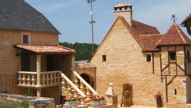 Un bâtiment en pierre avec un toit recouvert de tuiles, un escalier menant à un balcon et une petite fenêtre.