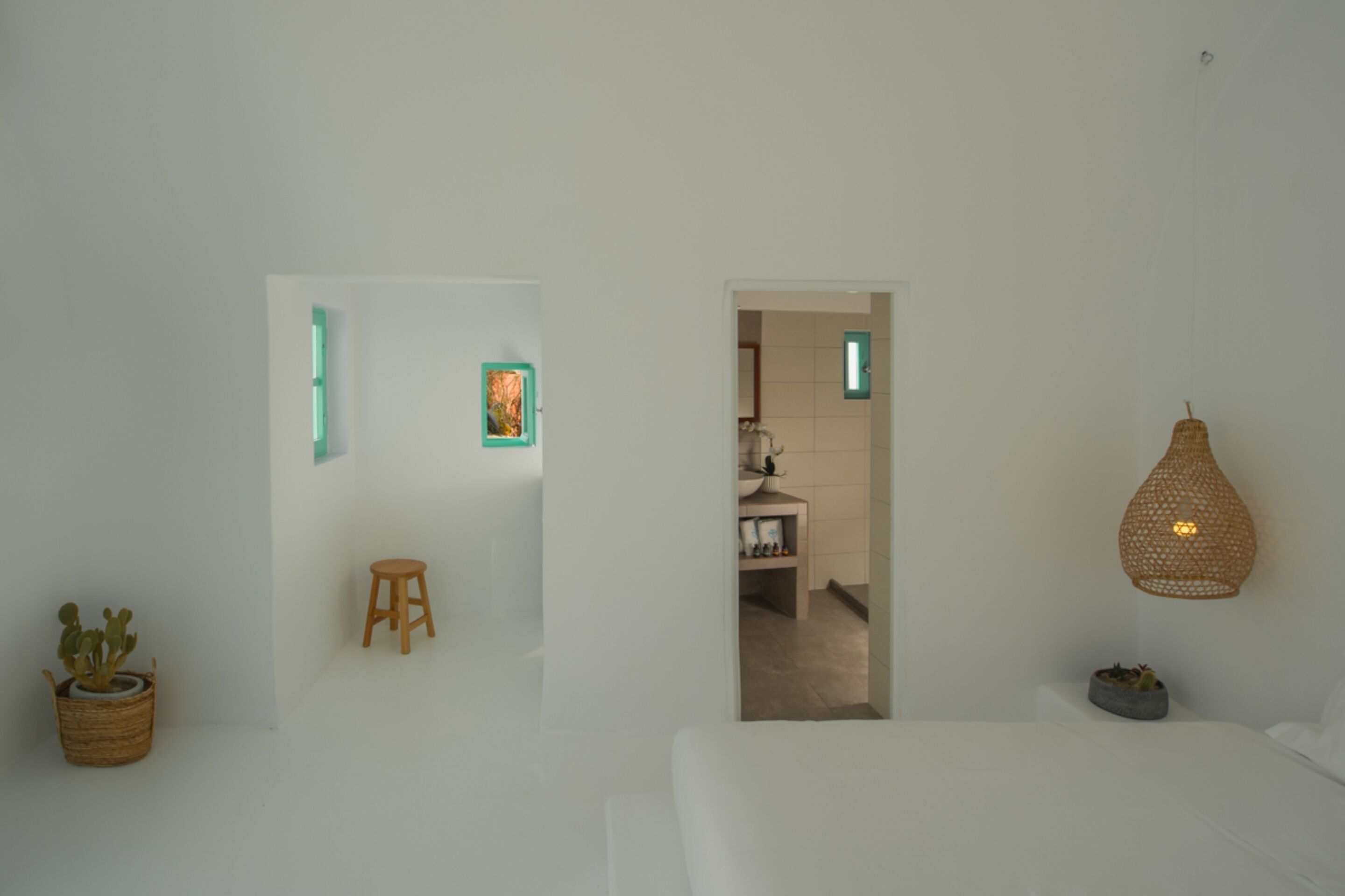 A minimalist room with a bed, a small stool, a potted plant, and a hanging light fixture.