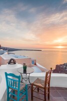 Terraza con vista al mar al atardecer, con una mesa y dos sillas.