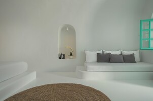 Una sala de estar moderna y minimalista con un sofá blanco, un tapete redondo tejido y una pequeña estantería con libros y una flor.