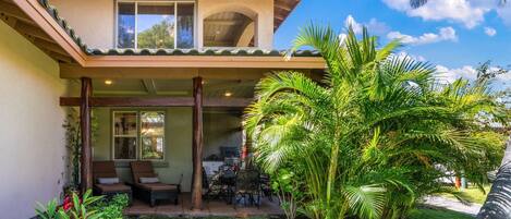 A two-story house with a covered patio, outdoor seating, and lush greenery.