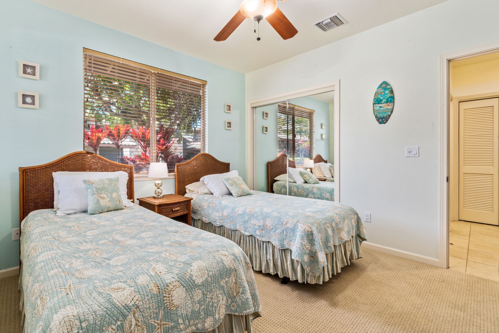 A bedroom with two beds, a ceiling fan, and a large window with blinds.