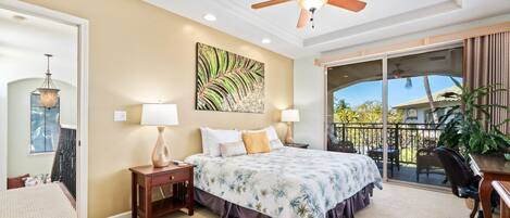 Un dormitorio con cama, dos mesitas de noche, ventilador de techo, ventana grande con vistas y balcón con una silla y planta.