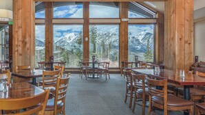Un restaurant doté de grandes fenêtres offrant une vue sur les montagnes, avec un décor intérieur en bois et différents types d’aménagements pour les places assises.