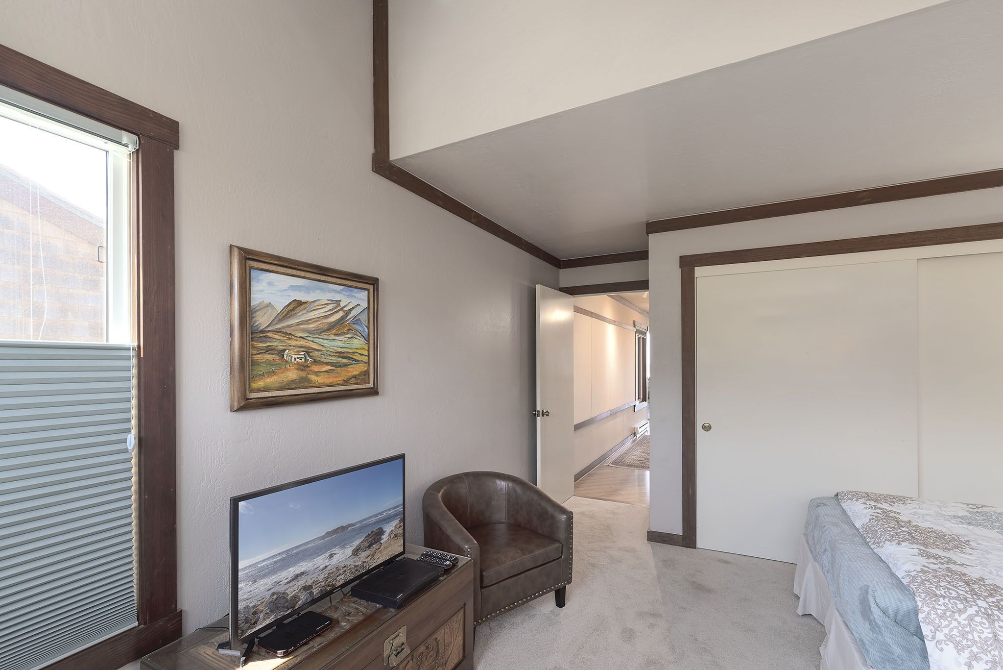 Een slaapkamer met een bed, een bureau met een computer, een stoel en een schilderij aan de muur.