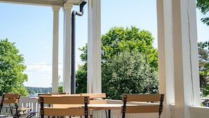 A covered outdoor seating area with white columns and wooden benches, overlooking a body of water and trees. - Boutique Hotel Willa Aria (Savonlinna)