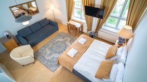 A hotel room with a bed, a sofa, a desk, a chair, a TV, and a window with curtains. - Boutique Hotel Willa Aria (Savonlinna)
