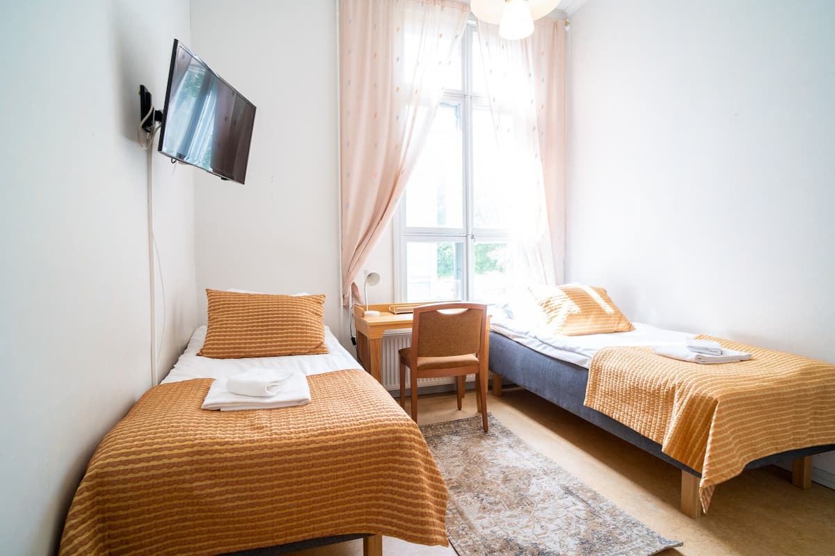 Une chambre avec deux lits, un bureau, une chaise et un téléviseur fixé au mur.