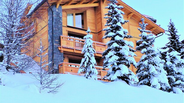 Un chalet en bois doté d’un balcon, entouré d’arbres couverts de neige.