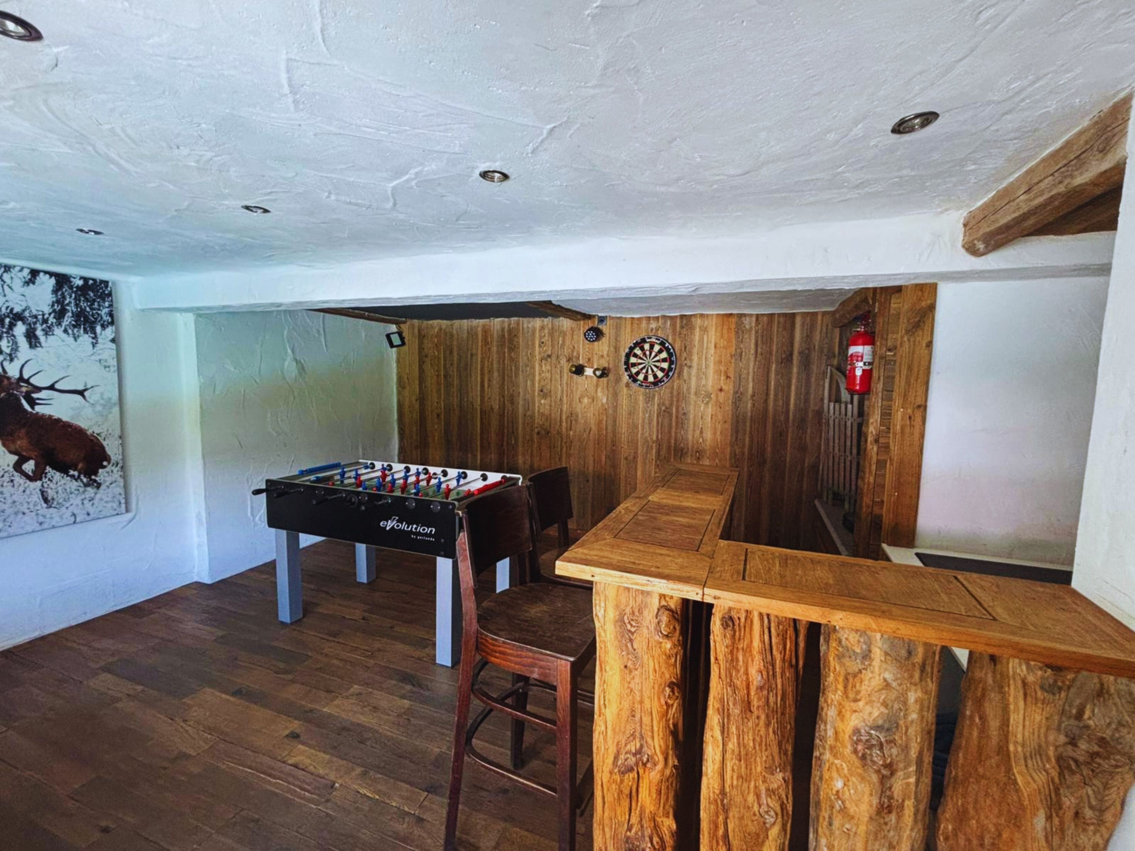 Una habitación con mesa de fútbol, dardos y una zona de bar de madera.