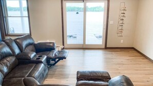 A spacious living room with a large sectional sofa, a small ottoman, and a view of a lake through a glass door.