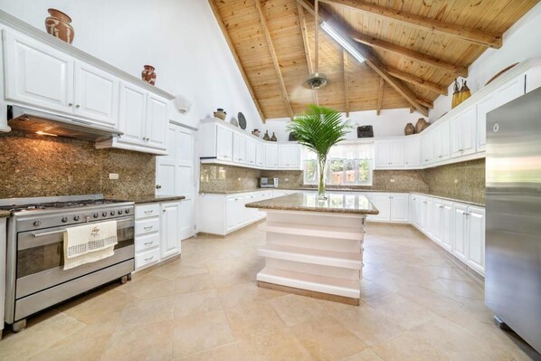 A spacious kitchen with white cabinets, a central island, a stove, and a refrigerator.