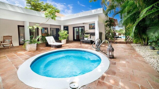 Un espace piscine extérieur moderne, doté d’un patio carrelé, de chaises longues et de plantes en pot.