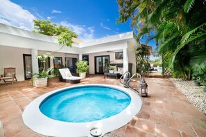 Un espace piscine extérieur moderne, doté d’un patio carrelé, de chaises longues et de plantes en pot.