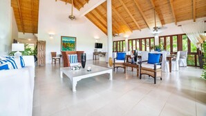 Un vaste espace de vie doté d’un haut plafond en bois, d’un canapé blanc, d’une table basse et d’un coin repas avec des chaises et une table.