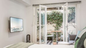 Un dormitorio con cama, televisor, calefacción y vistas a un jardín a través de un ventanal.