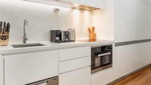 Una cocina moderna con armarios blancos, un lavamanos de acero inoxidable, una cafetera, un tostador y un horno empotrado.