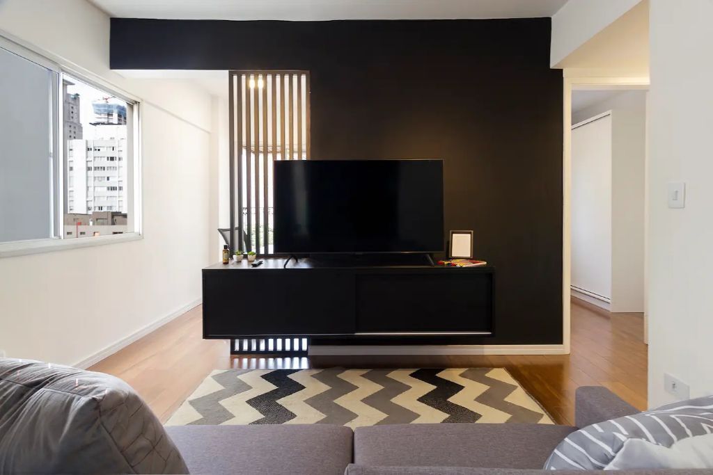 A modern living room with a large flat-screen TV on a black entertainment unit, a large window, and a chevron-patterned rug.