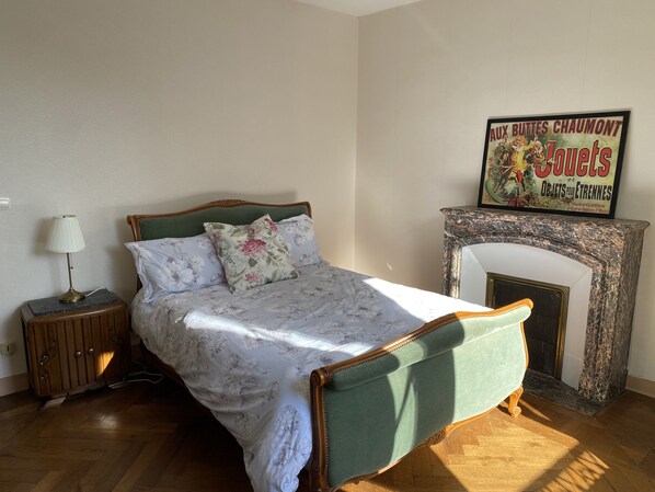 Un dormitorio con cama, mesita de noche, lámpara, chimenea y un cartel en la pared.