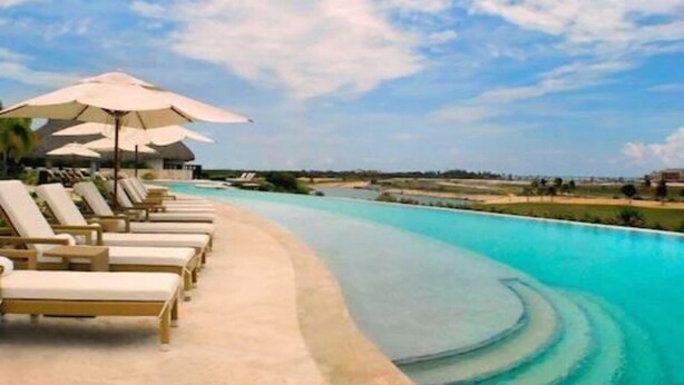 A poolside area with lounge chairs and umbrellas, a clear sky, and a calm pool. - Golden Bear Lodge and Spa (Punta Cana)