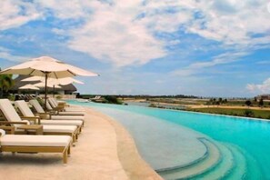 A poolside area with lounge chairs and umbrellas, a clear sky, and a calm pool. - Golden Bear Lodge and Spa (Punta Cana)