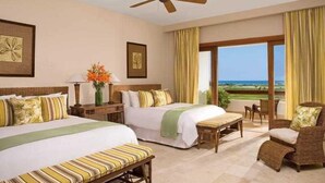 A hotel room with two beds, a ceiling fan, a view of the ocean, and a balcony with a chair. - Golden Bear Lodge and Spa (Punta Cana)