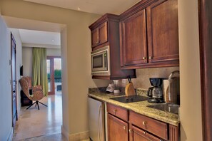 A kitchen with wooden cabinets, a microwave, a coffee maker, and a chair. - Golden Bear Lodge and Spa (Punta Cana)