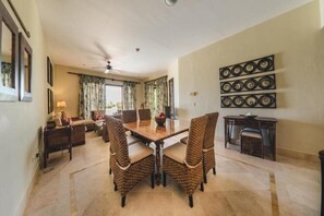 Un comedor con mesa de madera, sillas de mimbre, ventilador de techo y un adorno en la pared.