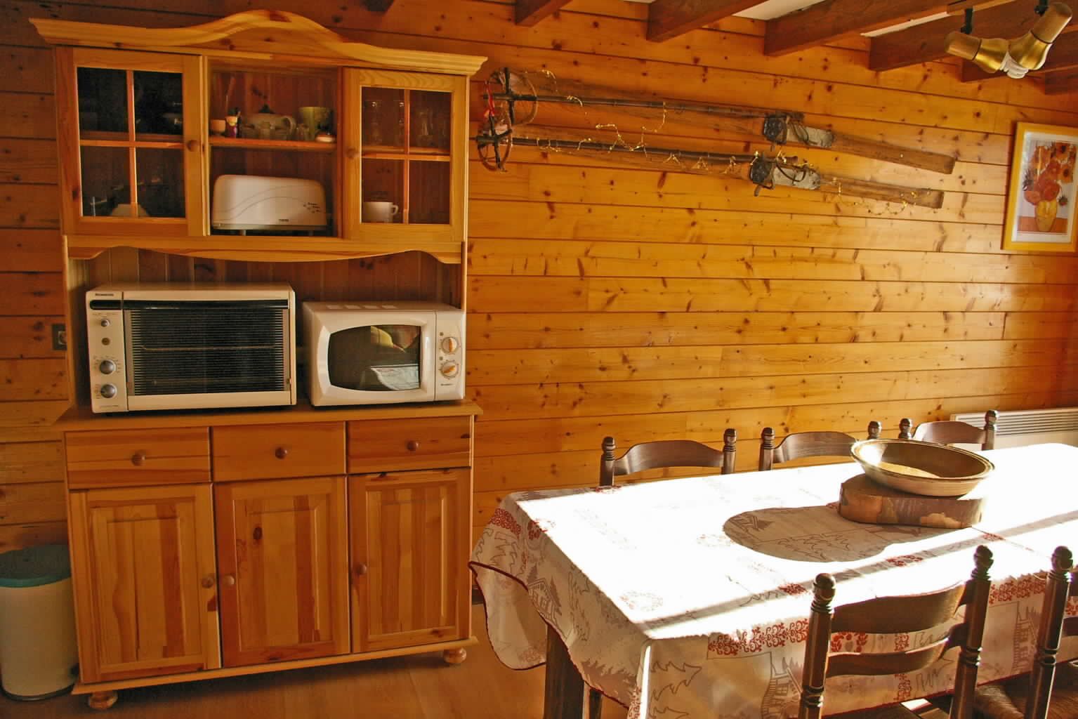A wooden cabin interior with a dining table, chairs, a cabinet with glass doors, and a wall-mounted bicycle.