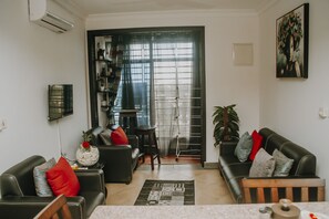A living room with a black sofa, a coffee table, and a TV mounted on the wall.